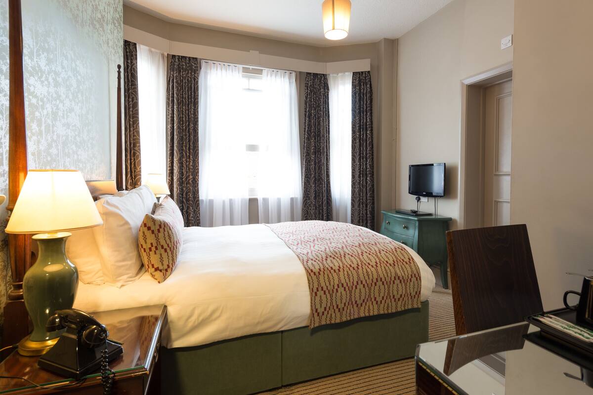 Une chambre d’hôtel comprenant un lit, un bureau avec une lampe, un téléphone, une télévision et une chaise.