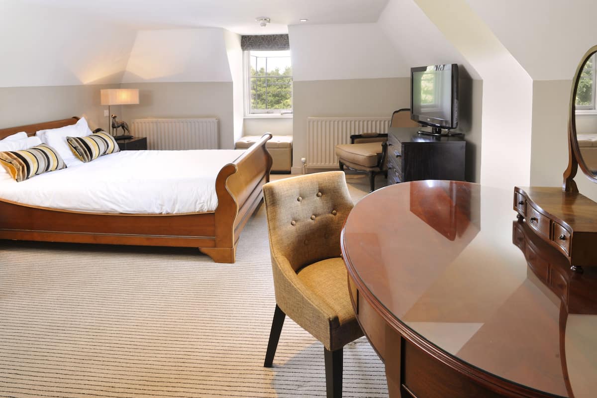 Une chambre d’hôtel avec un grand lit, un bureau en bois, une chaise, une télévision et une fenêtre donnant sur des arbres.