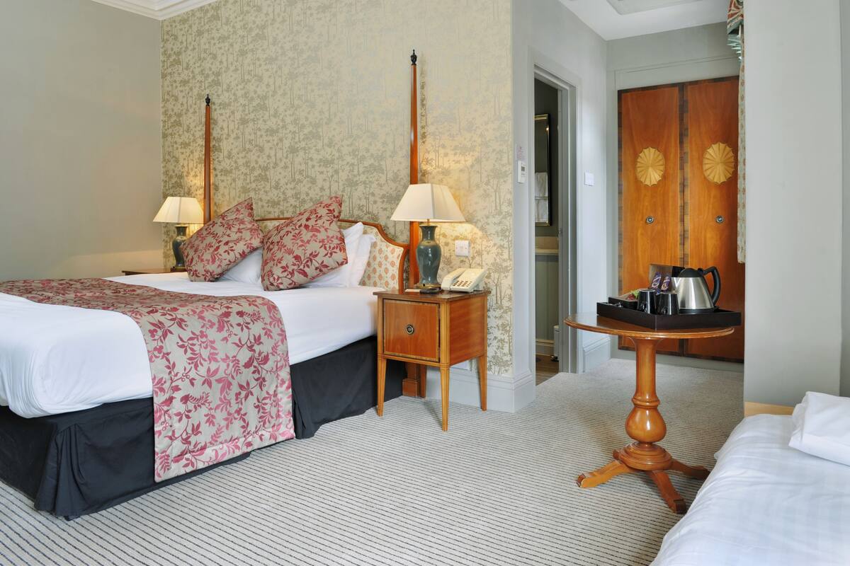 Une chambre d’hôtel avec un grand lit, deux tables de chevet, une petite table d’appoint, une armoire en bois et une petite table ronde avec un plateau.