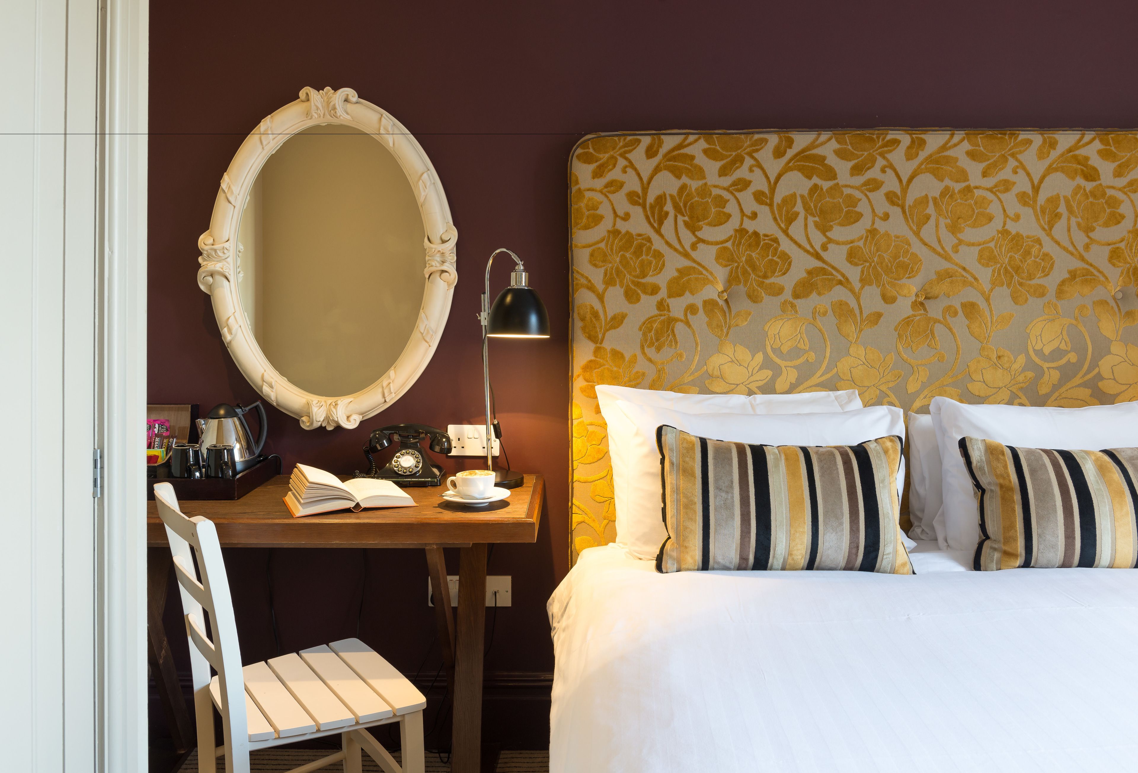A hotel room with a bed, a desk with a lamp, a chair, a mirror, and a telephone.
