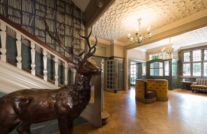 Una imponente escalera con una gran escultura de un alce, un candelabro y una zona de estar acogedora con chimenea.