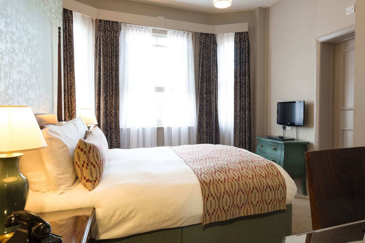 Une chambre d’hôtel avec un lit, un bureau avec une télévision et une chaise.