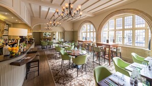 Un restaurante espacioso con techos altos, candelabros y ventanas amplias.