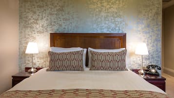 A neatly made bed with a patterned bedspread and pillows, flanked by two bedside tables with lamps and a rotary phone.