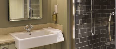 A bathroom with a white sink, a mirror, a glass-enclosed shower, and a towel hanging on the sink.