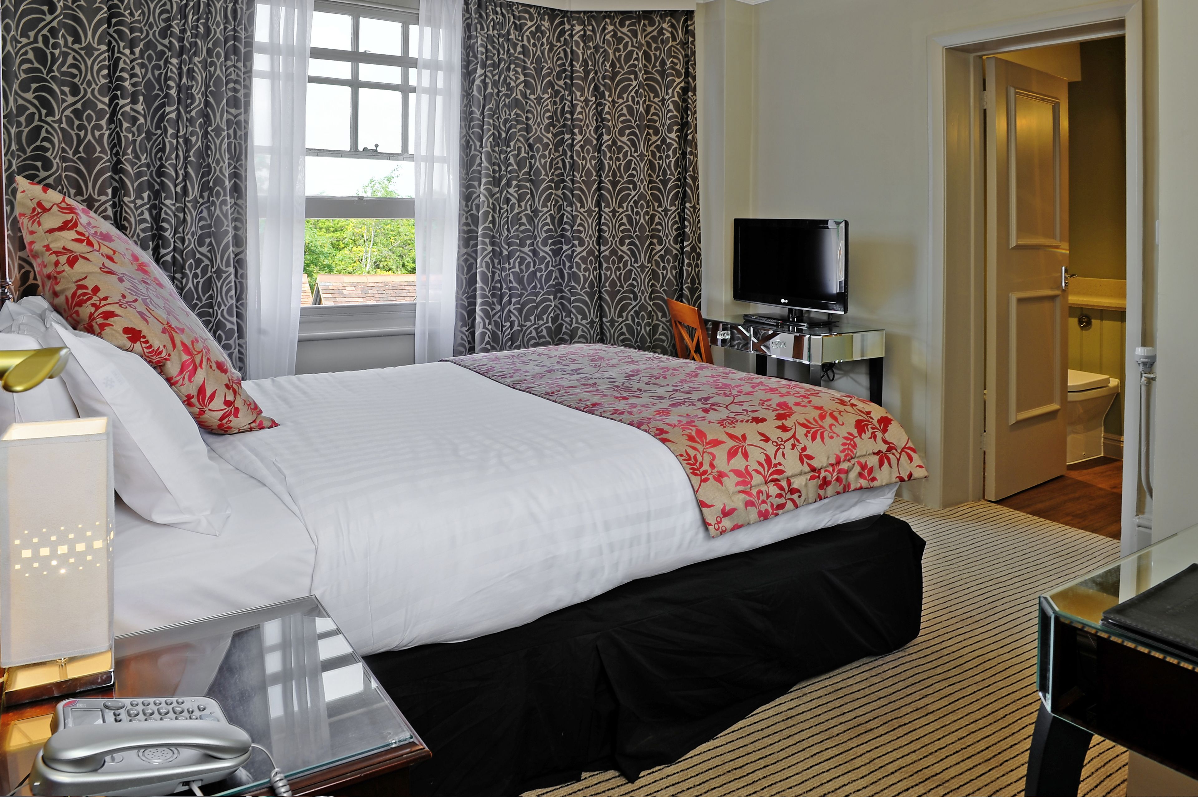 A hotel room with a bed, a television, a desk with a computer, and a bathroom visible through an open door.