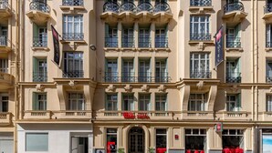 Un hotel de varios pisos con estilo arquitectónico clásico, con balcones y barandillas ornamentales, ventanas amplias y una entrada destacada con un letrero rojo.
