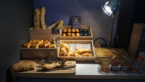 Una exposición de productos horneados varios, incluyendo pan, cruasanes y muffins, con un letrero que indica 'La Madeleine' y una lámpara al fondo.