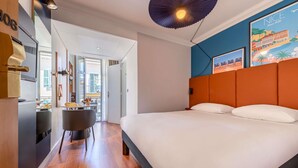 Habitación de hotel con cama, escritorio, silla, lámpara en el techo y vista al exterior.