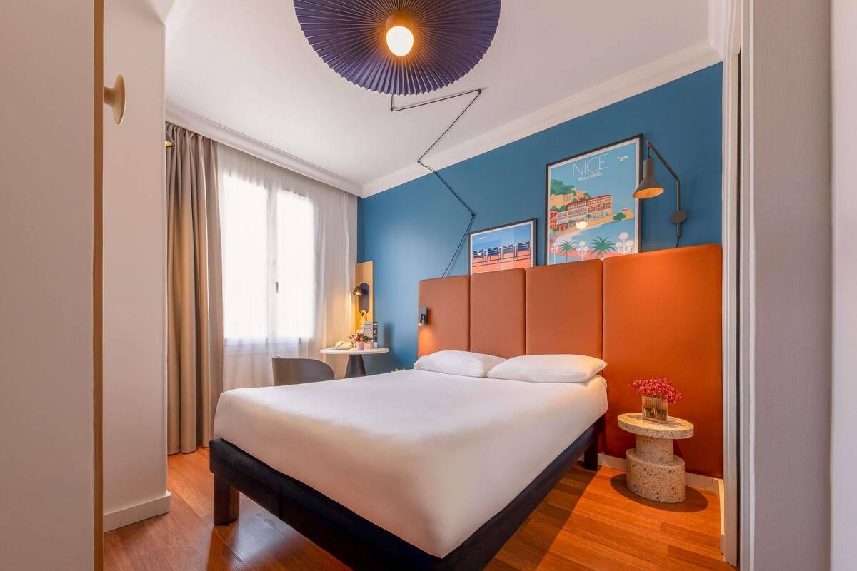 A modern hotel room with a large bed, a desk, and a nightstand.