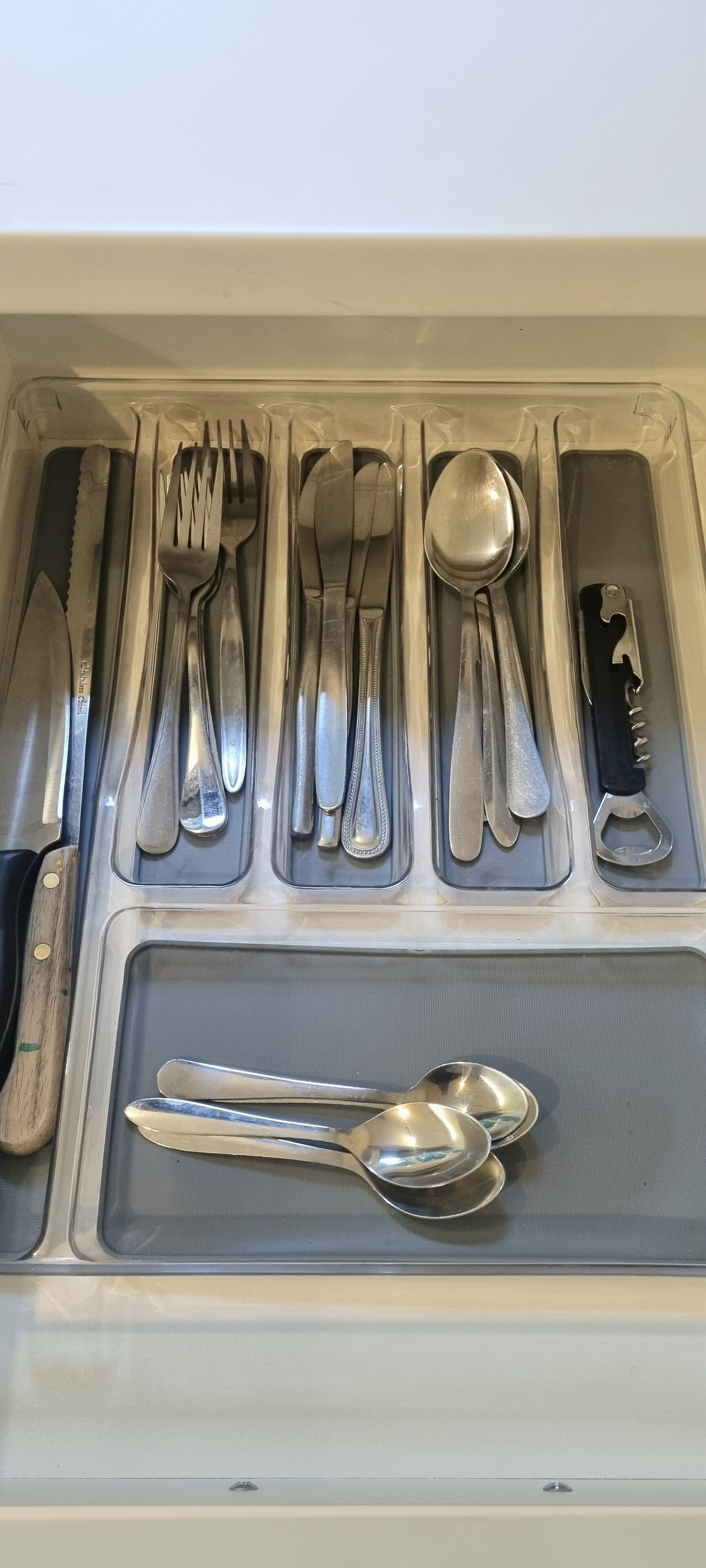 A drawer with neatly arranged cutlery including forks, knives, spoons, and a bottle opener.