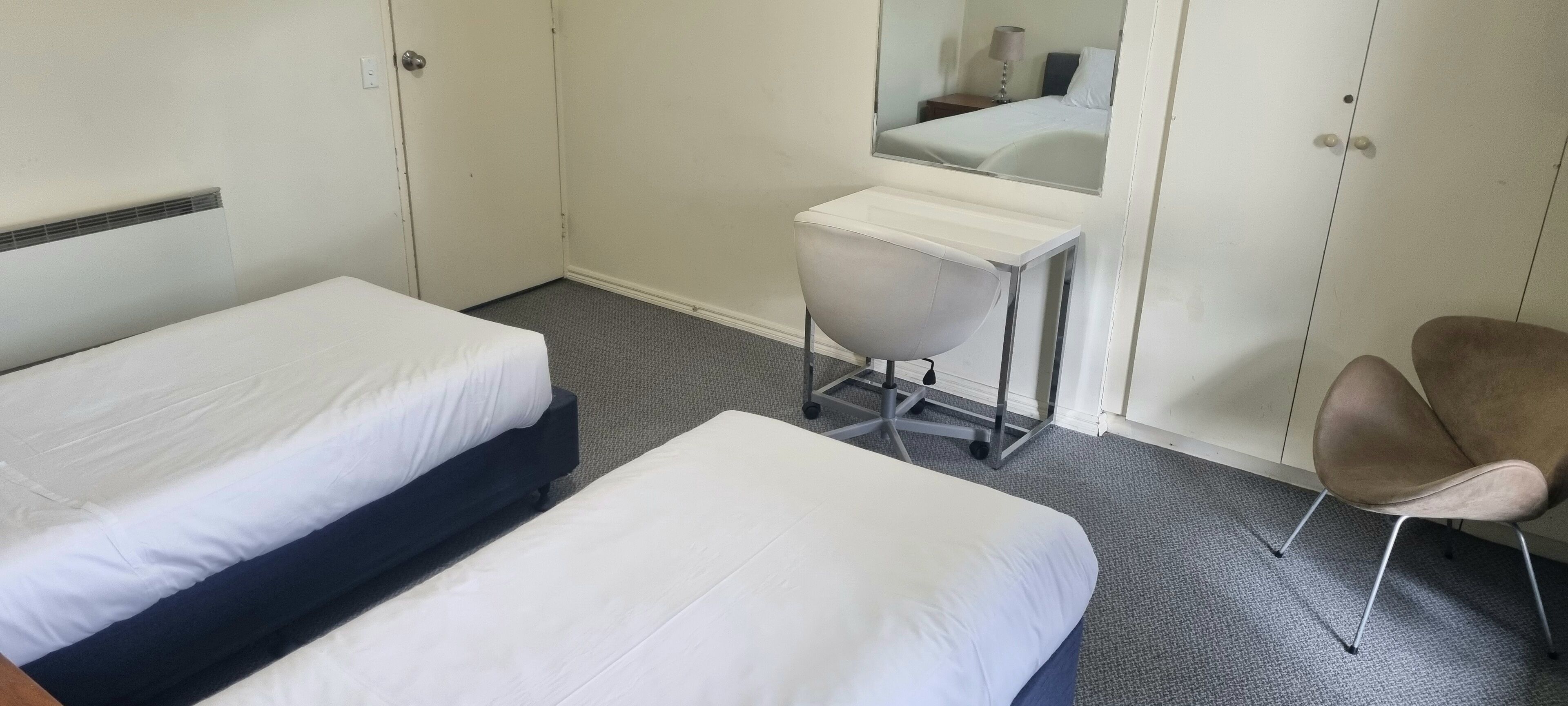 Une chambre d’hôtel avec deux lits simples, un bureau avec une chaise, un miroir et une armoire.