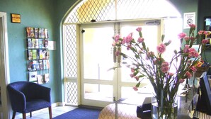 Ein Empfangsbereich mit blauem Sessel, einer Glasvase mit rosa Blumen, einer Pinwand mit Broschüren und einem gefliesten Boden.