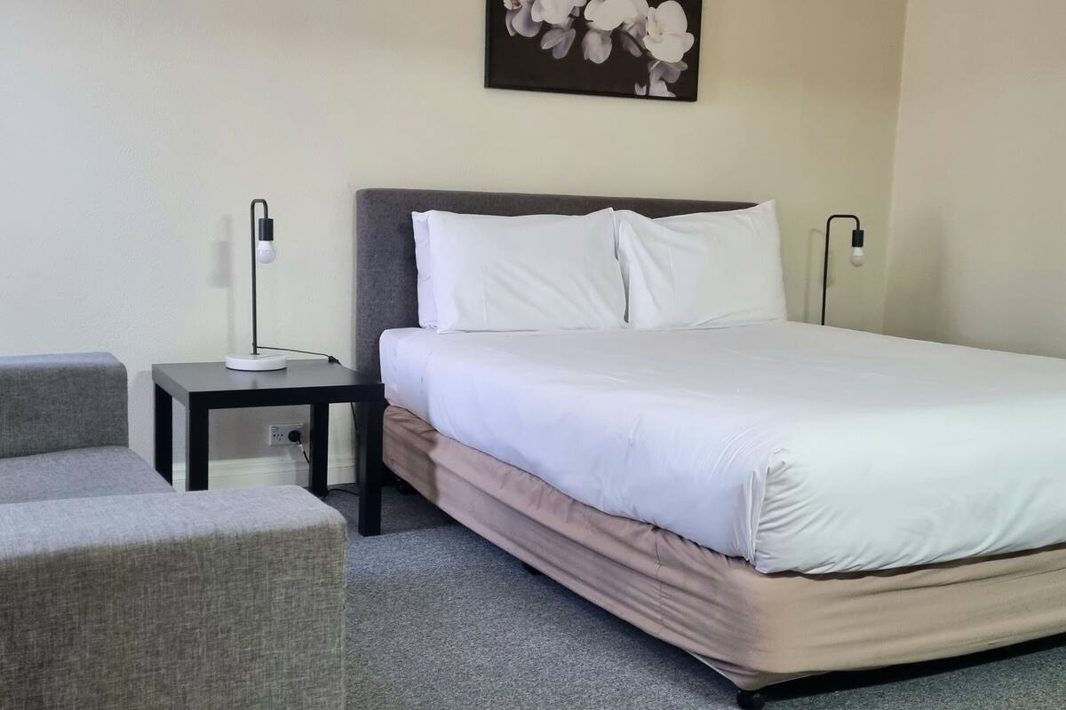 Une chambre d’hôtel avec un lit, une table de chevet, une lampe et une chaise.