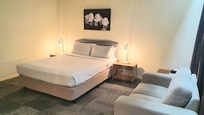 Ein Hotelzimmer mit einem Bett, zwei Nachttischen mit Lampen, einer kleinen Couch und einem Wandbild.