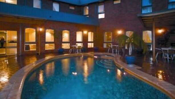 Ein Hotelinnenhof mit Schwimmbad, Sitzgelegenheiten im Freien und einer Ziegelhausfassade.