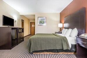 A hotel room with a bed, a TV, a microwave, a desk with a lamp, and a door leading to another room.