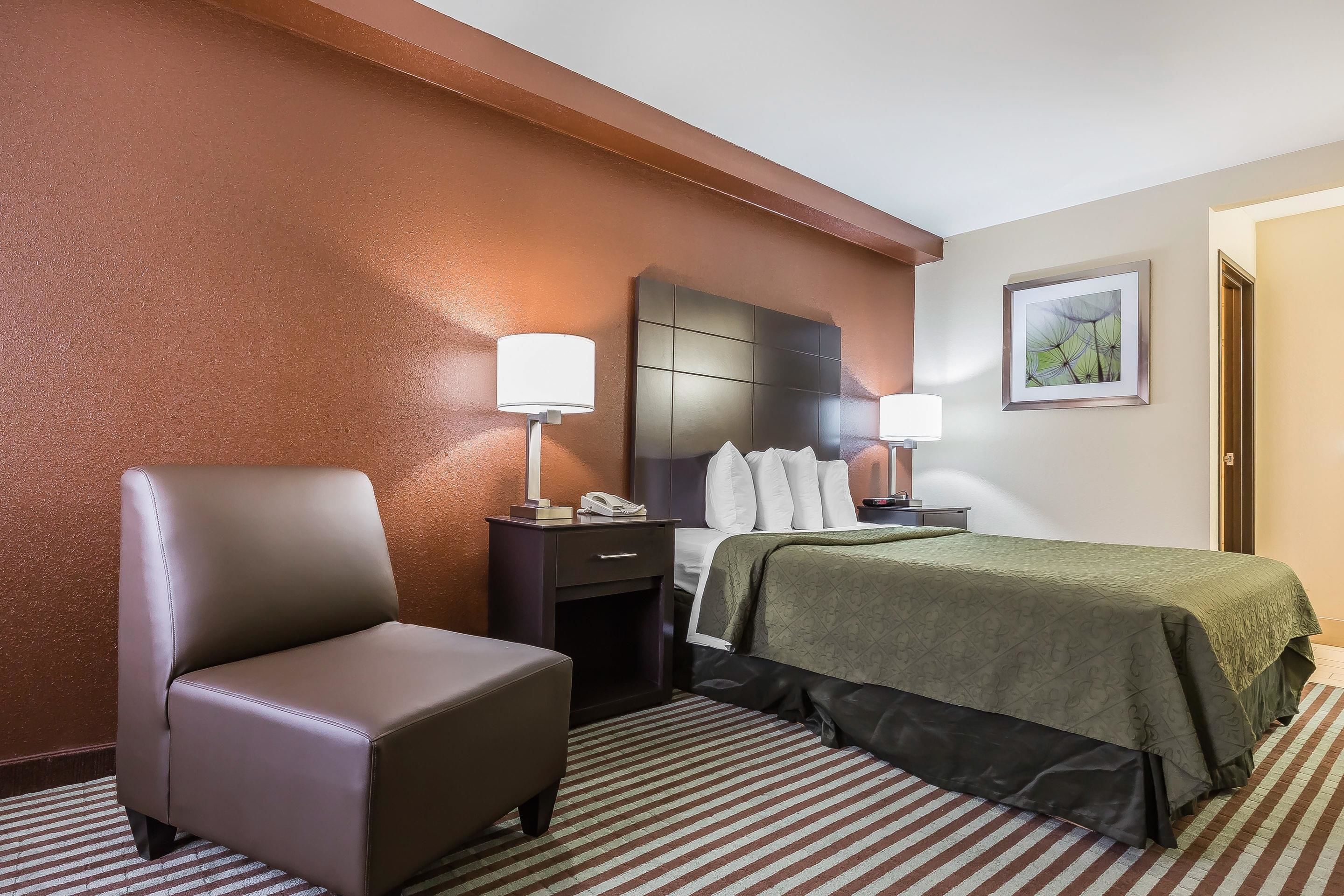 A hotel room with a large bed, a chair, a nightstand, and a framed picture on the wall.