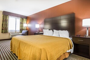 A hotel room with a large bed, two bedside tables with lamps, a chair, and a window with curtains.
