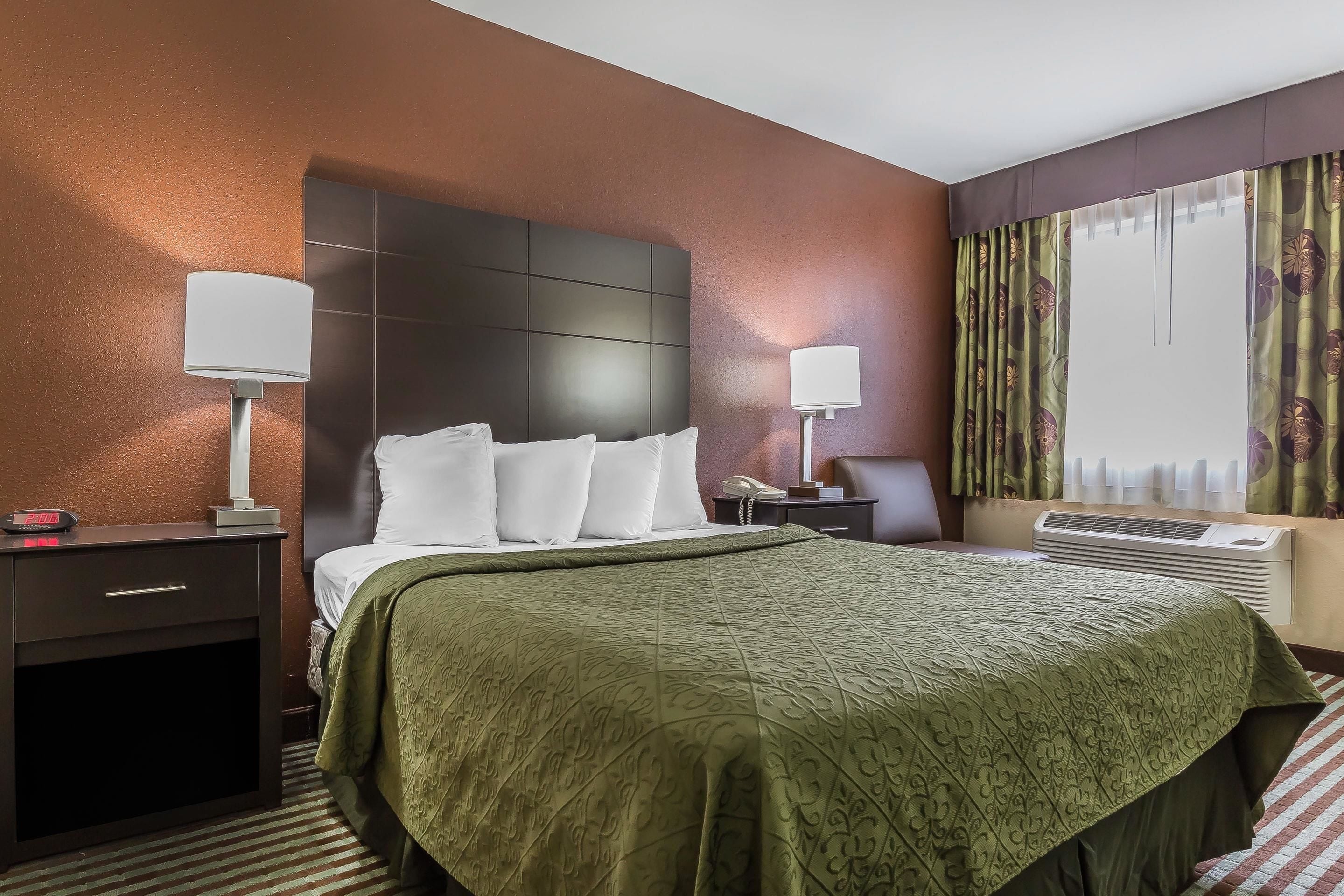 A hotel room with a large bed, two bedside tables with lamps, a nightstand, a desk with a telephone, and a window with curtains.