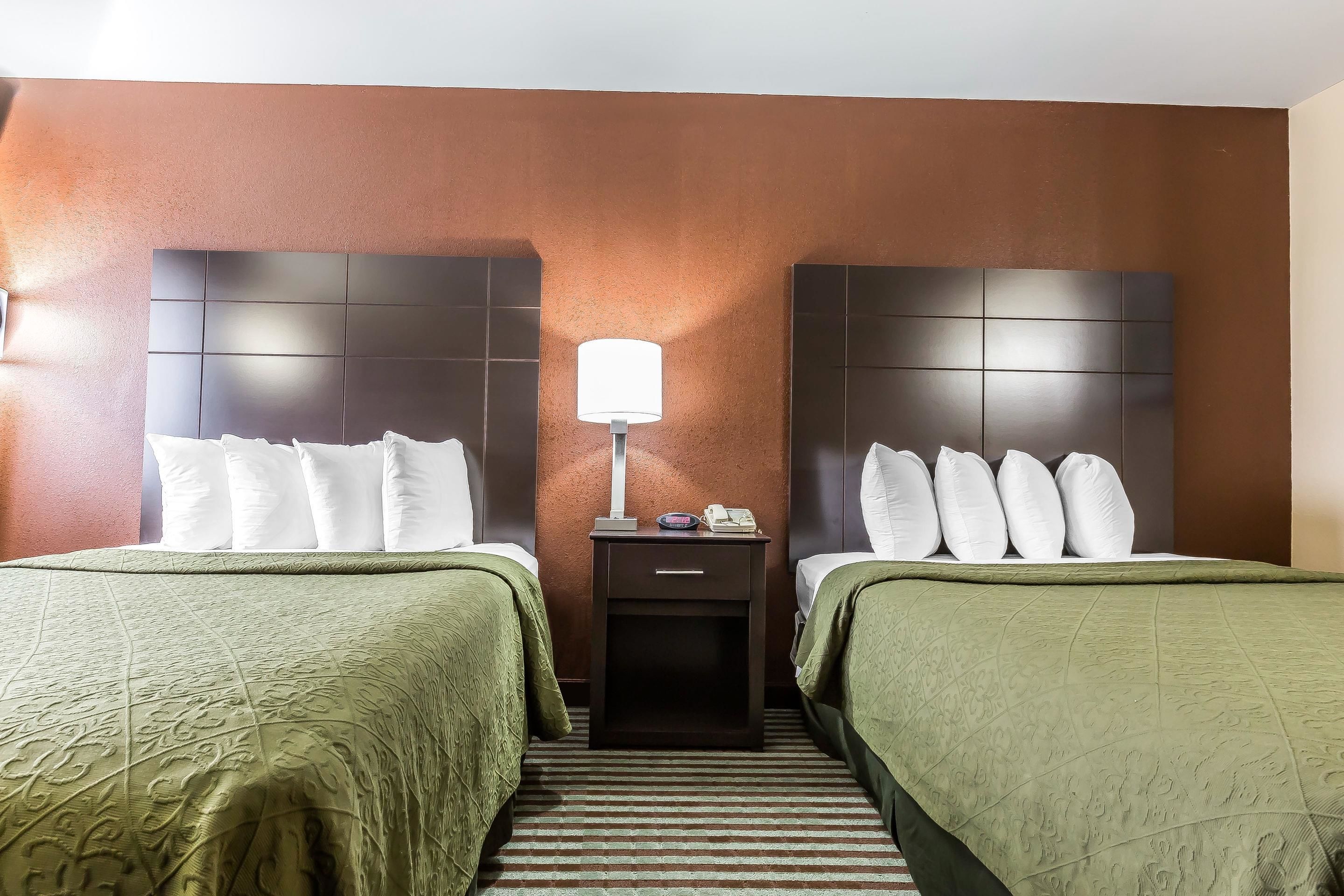 A hotel room with two beds, a nightstand with a lamp, and a striped carpet.