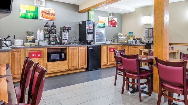 A modern kitchen with wooden cabinets, a refrigerator, a coffee machine, and a microwave. There are red chairs and a table in the dining area. - Quality Inn Mount Vernon, IL (Mount Vernon)