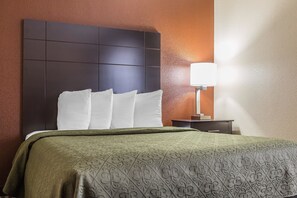 A hotel room with a large bed, a dark headboard, a bedside table with a lamp, and a wall with a textured finish.
