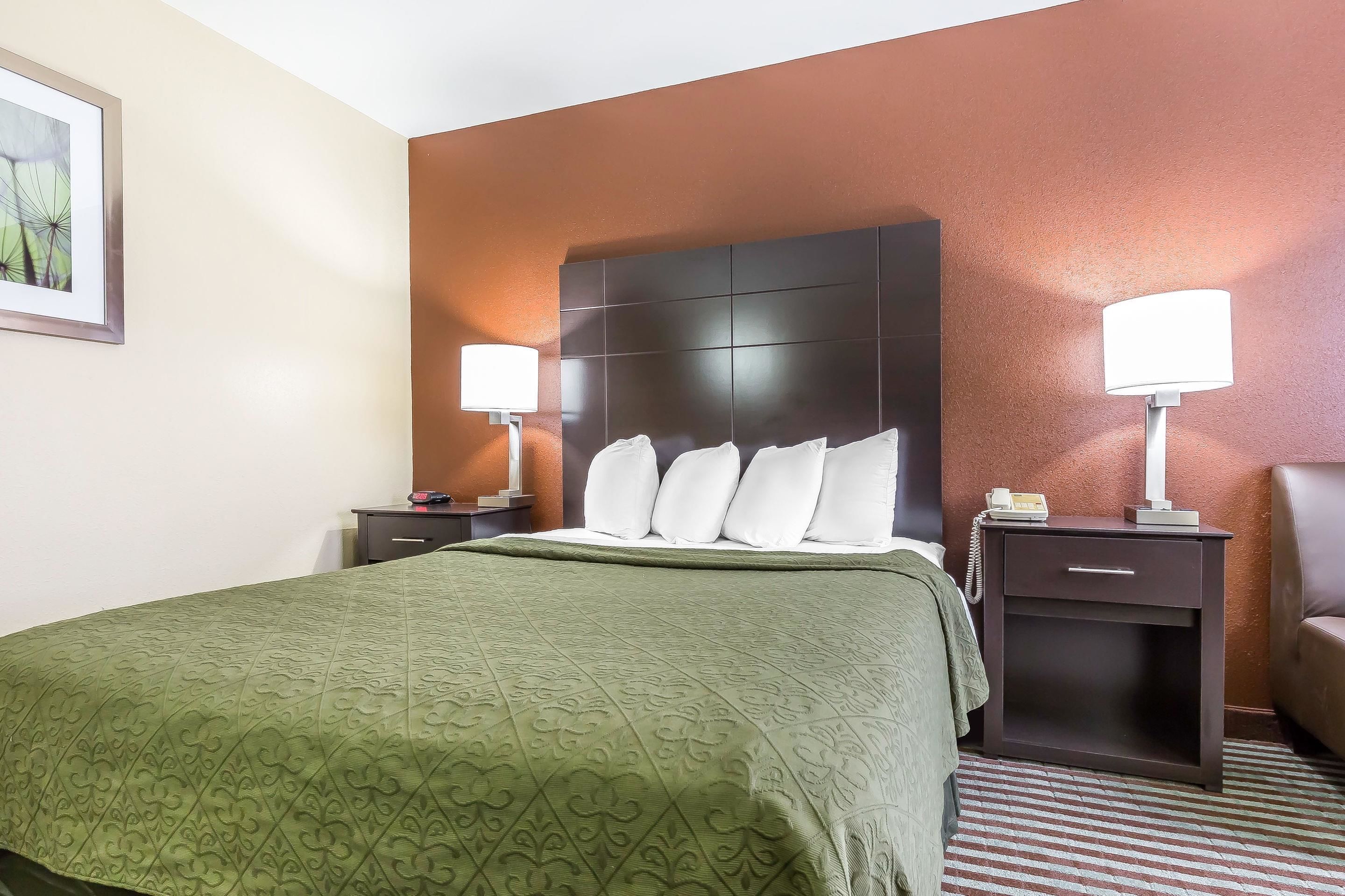 A hotel room with a large bed, two bedside tables with lamps, a nightstand, and a brown leather armchair.