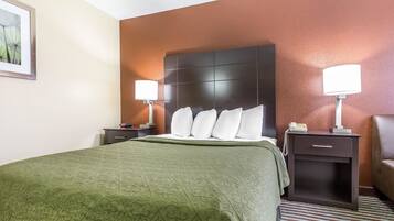 A hotel room with a large bed, two bedside tables with lamps, a nightstand, and a brown leather armchair.