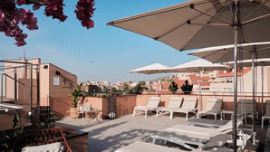 Terraço no telhado com cadeiras de descanso, guarda-sóis e plantas em vasos.