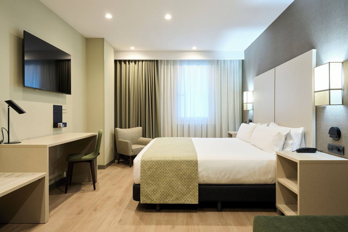 Habitación de hotel moderna con cama, escritorio, silla y televisor montado en la pared.