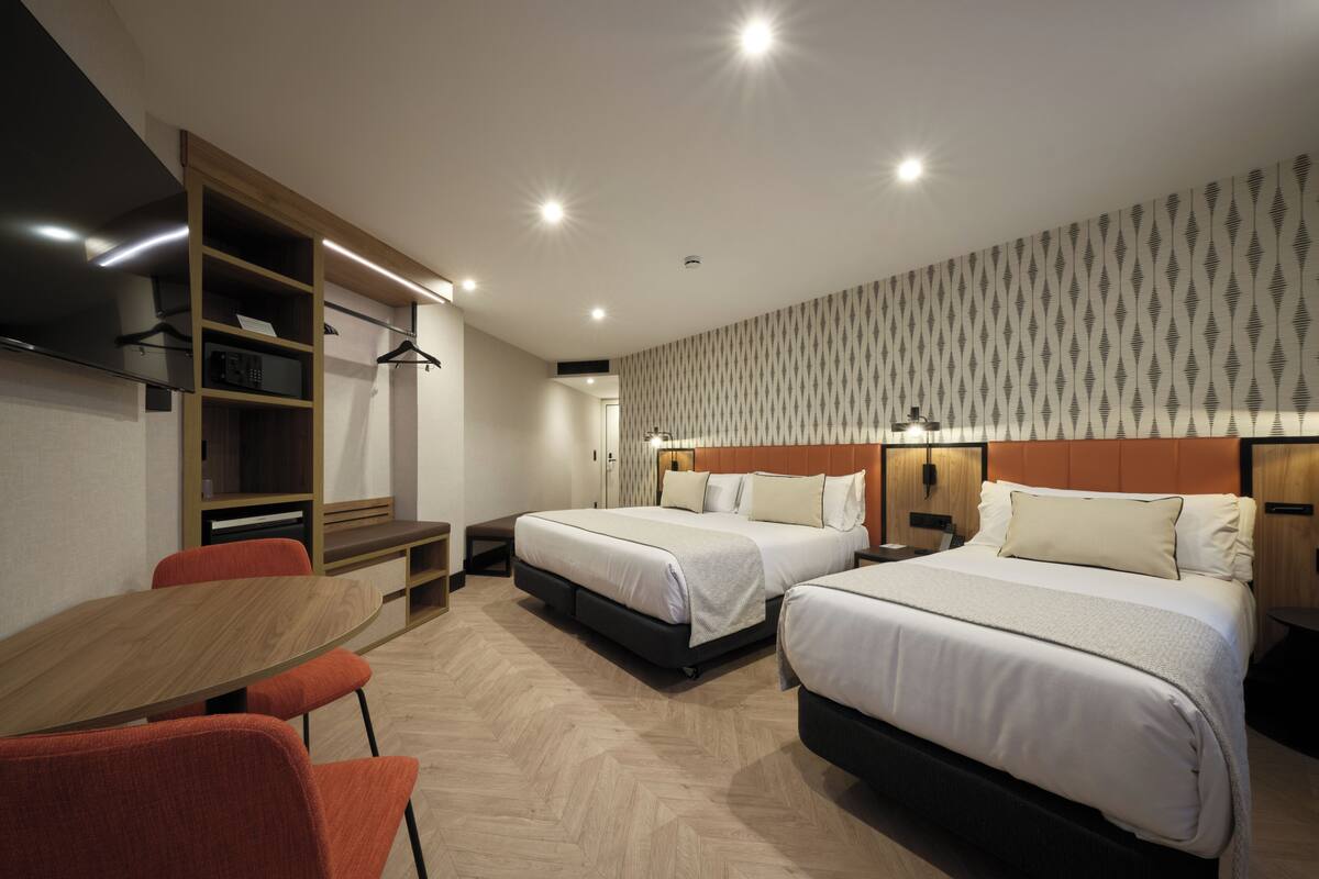 Habitación de hotel con dos camas, un escritorio de madera y un armario.