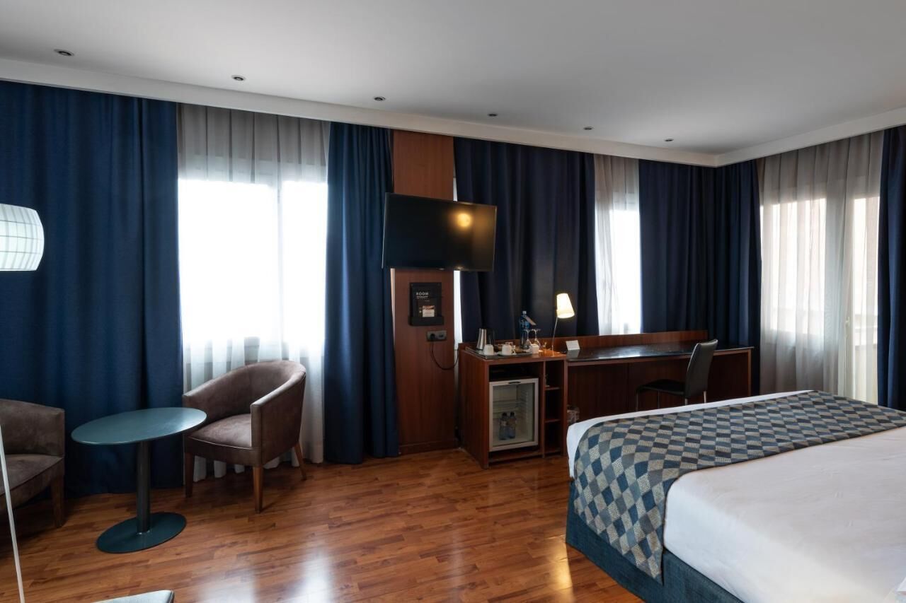 A hotel room with a bed, desk, chair, and a small table.