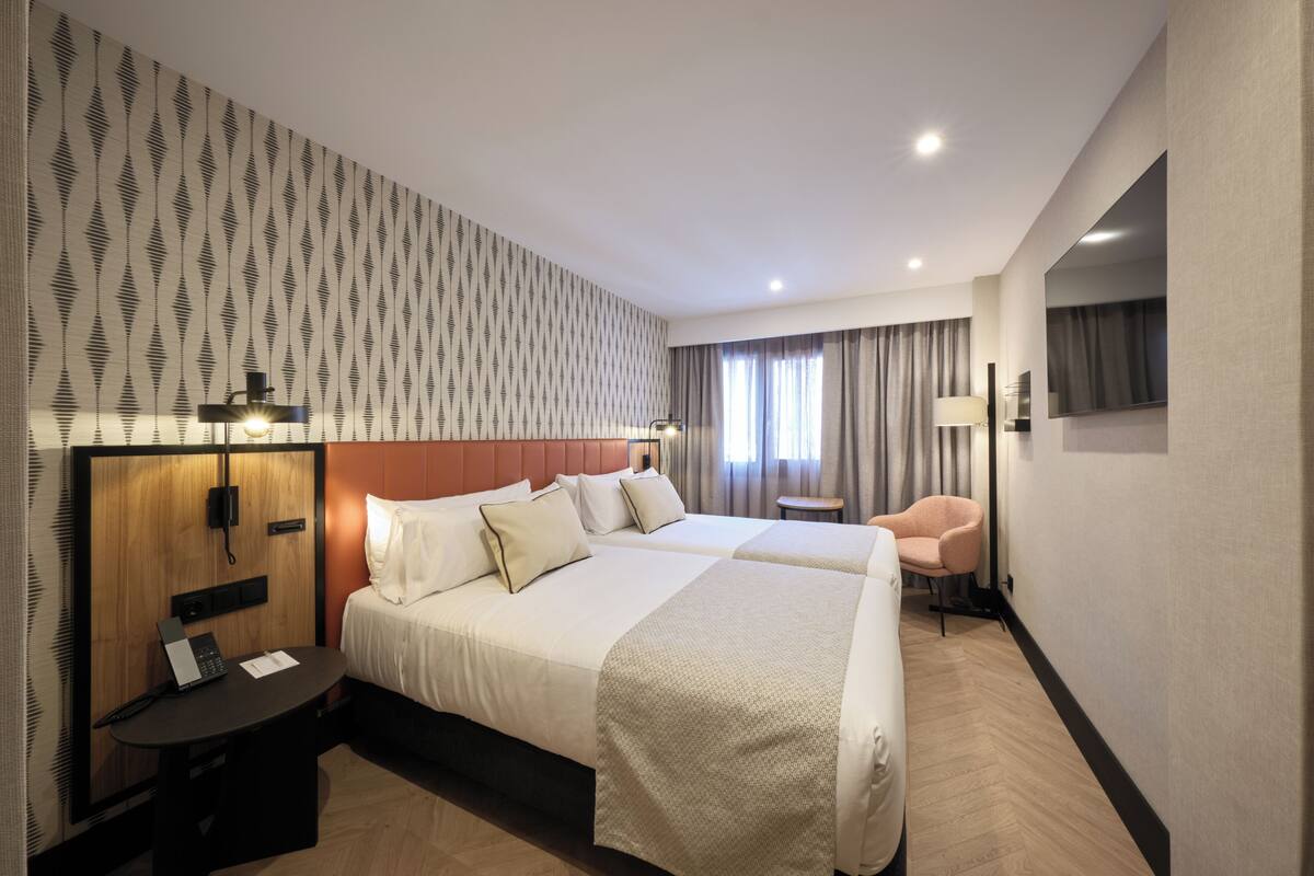 Habitación de hotel con dos camas, un escritorio con teléfono, una silla y una televisión.