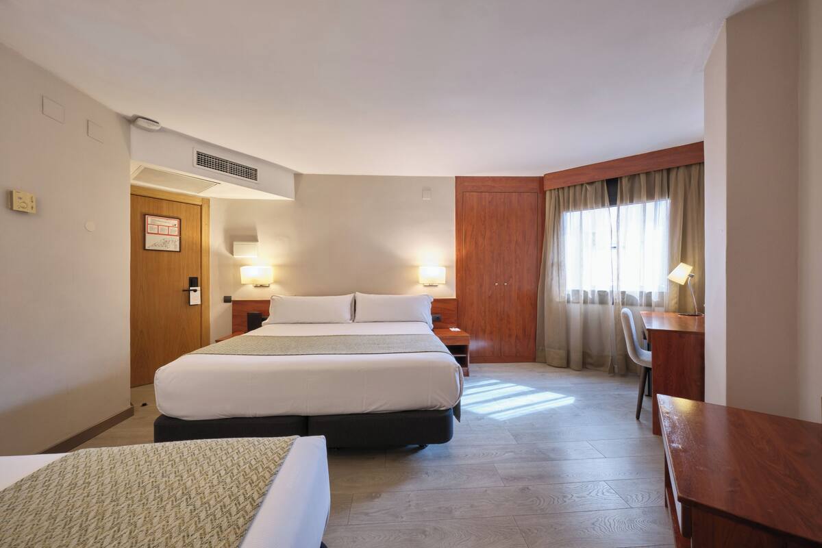 Una habitación de hotel con una cama grande, mesitas de noche, un escritorio y una silla.