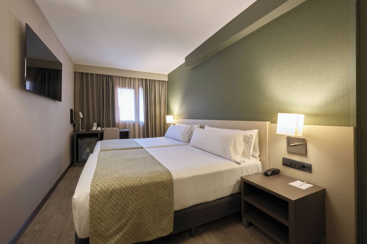 Habitación de hotel con dos camas, un escritorio, un televisor y una lámpara.