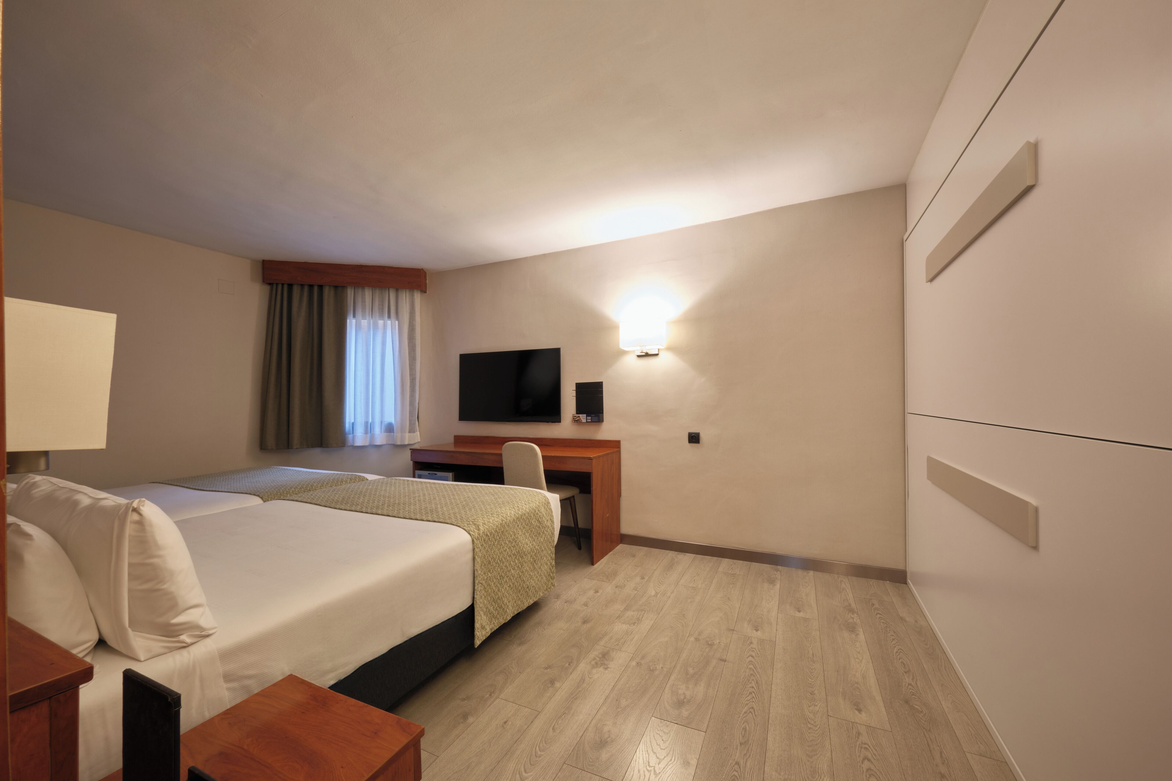 Una habitación de hotel con dos camas, un escritorio, un televisor y una lámpara fijada a la pared.