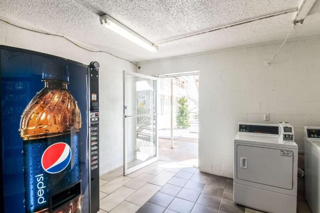 A room with a large Pepsi vending machine, a glass door leading outside, and a washing machine.