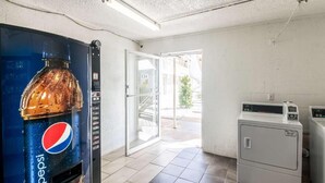 A room with a large Pepsi vending machine, a glass door leading outside, and a washing machine. - Whitten Inn (Clinton)