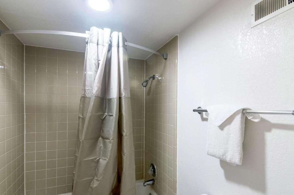 A shower with a curtain, a towel rack with a towel, and a vent on the wall.