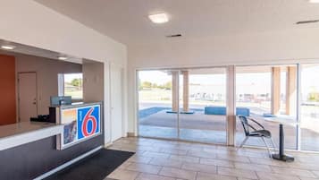 A hotel reception area with a reception desk, a large glass door leading outside, and a view of the parking lot.
