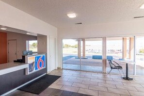 A hotel reception area with a reception desk, a large glass door leading outside, and a view of the parking lot.