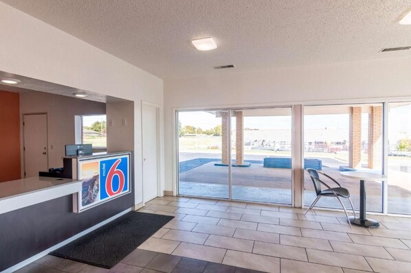 A hotel reception area with a reception desk, a large glass door leading outside, and a view of the parking lot.