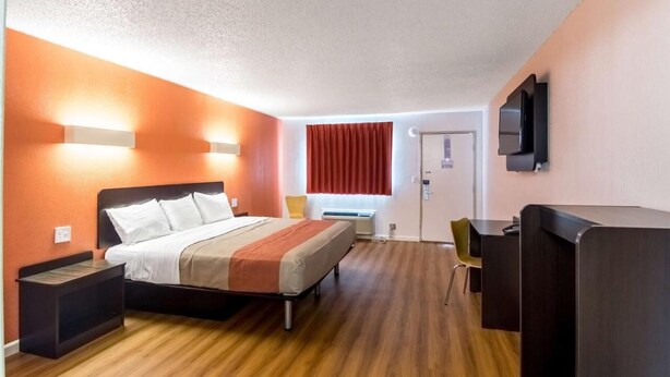A hotel room with a bed, bedside tables, a desk, a chair, a TV, and a window with curtains.