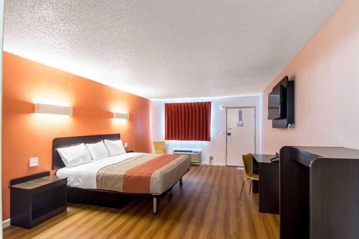 Habitación de hotel con cama, mesitas de noche, escritorio, silla, televisor y ventana con cortinas.