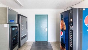 Un pasillo con una puerta azul, un refrigerador y una máquina expendedora.