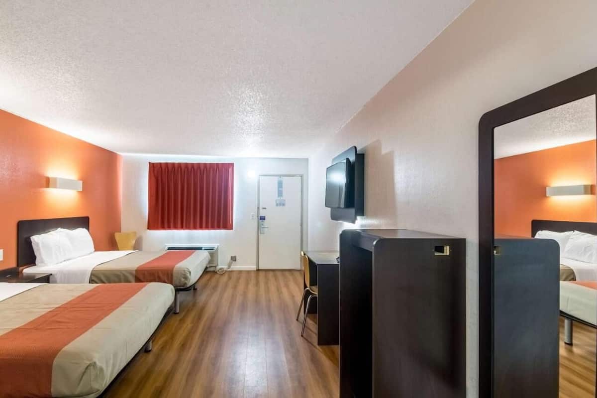 Habitación de hotel con dos camas, un escritorio, una silla, un televisor y un espejo.