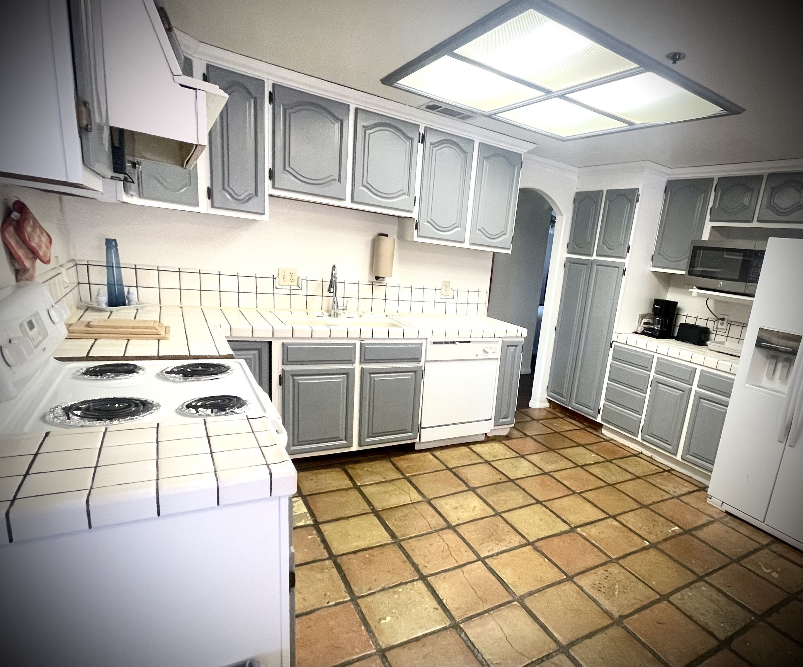 Una cocina con armarios blancos, estufa, microondas y lavavajillas.
