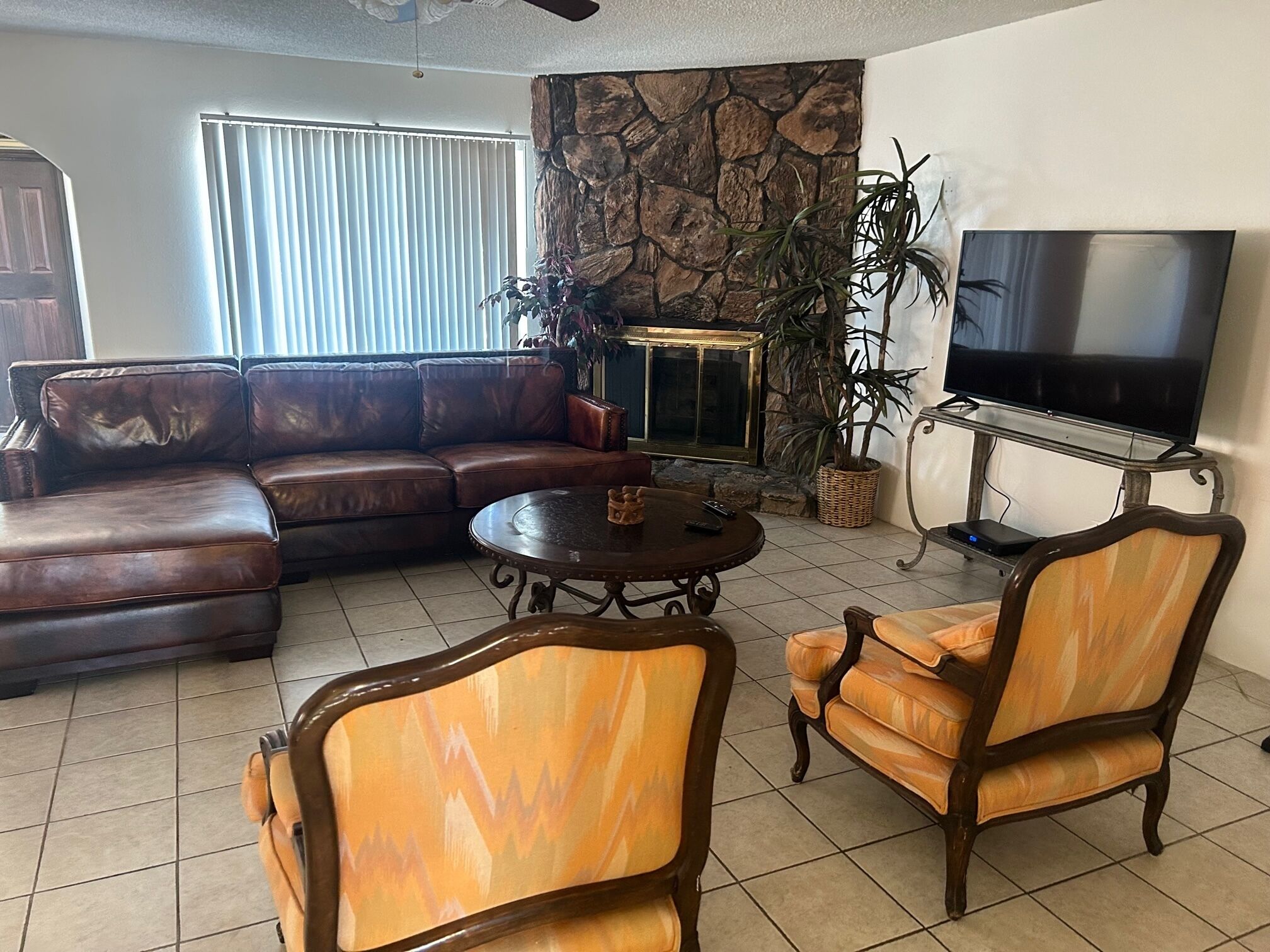 A living room with a sectional sofa, a coffee table, two armchairs, a television, and a stone accent wall.