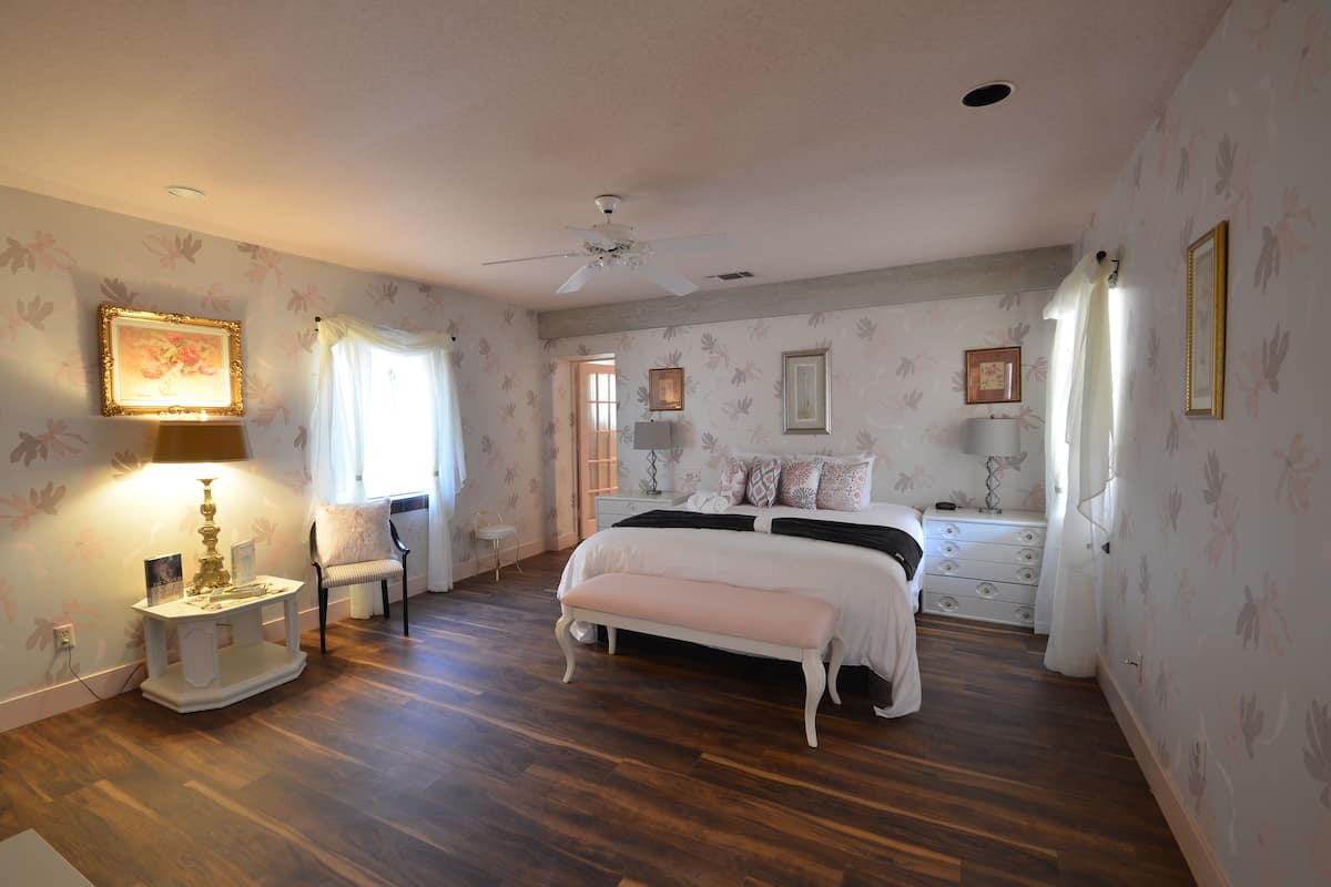 Une chambre à coucher comprenant un lit, des tables de chevet, une chaise, un bureau et un ventilateur de plafond.